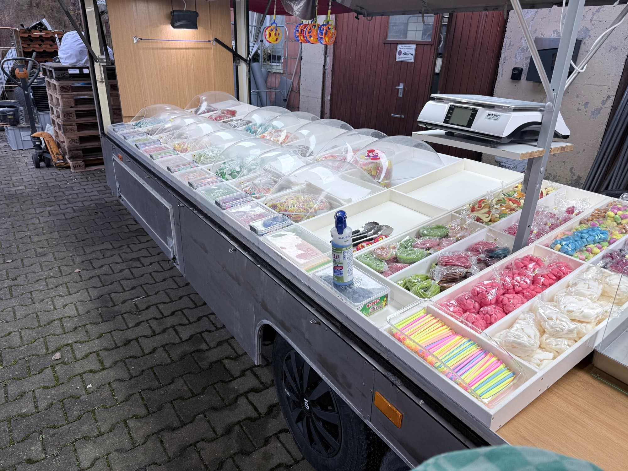 Süßwarentheke mit Schalen voller Fruchtgummi unter Klarsichthauben und einer Waage