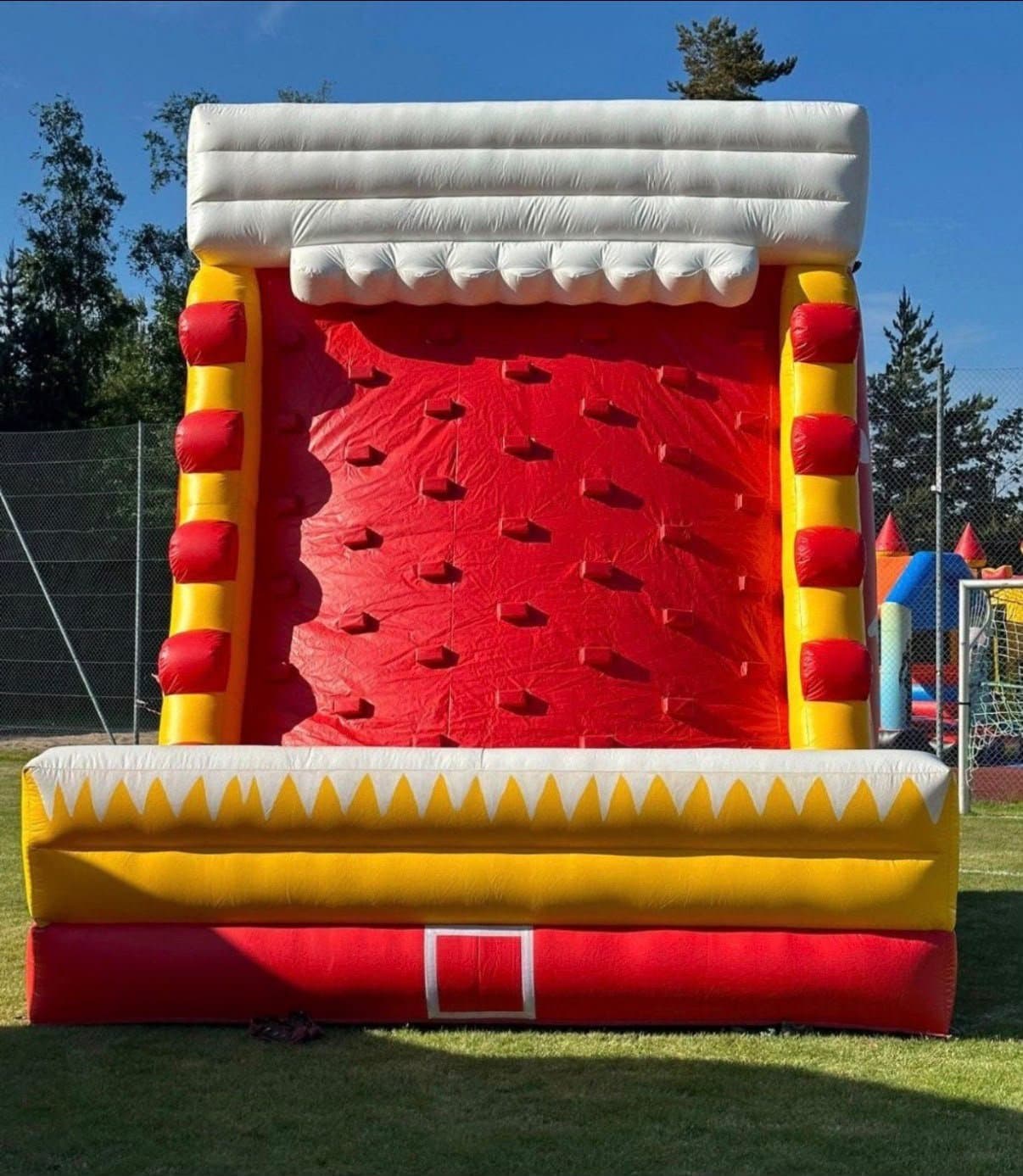Aufblasbare Kletterwand in Rot, Gelb und Weiß auf Rasen, von vorne